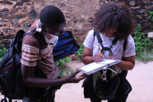 Two people with backpacks and other gear working together on a clipboard taking notes.