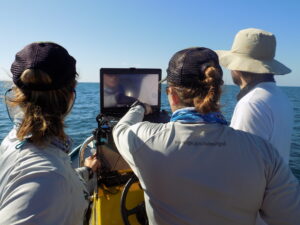 Three people overlooking water looking at a computer.