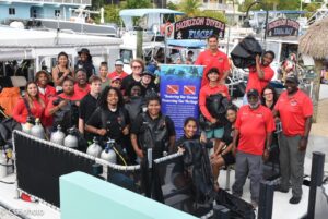 Large group of young people on boat and dock around "Youth Diving With a Purpose" signs. Some are in dive gear and others are wearing red DWP t shirts.