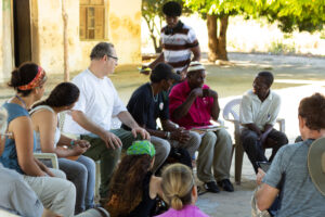 Group of people sitting in a circle listening to a person speak in the center.