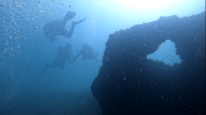 Three divers swimming underwater next to rock formation.