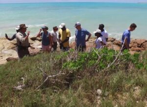 Group of people standing and speaking together on the beach.