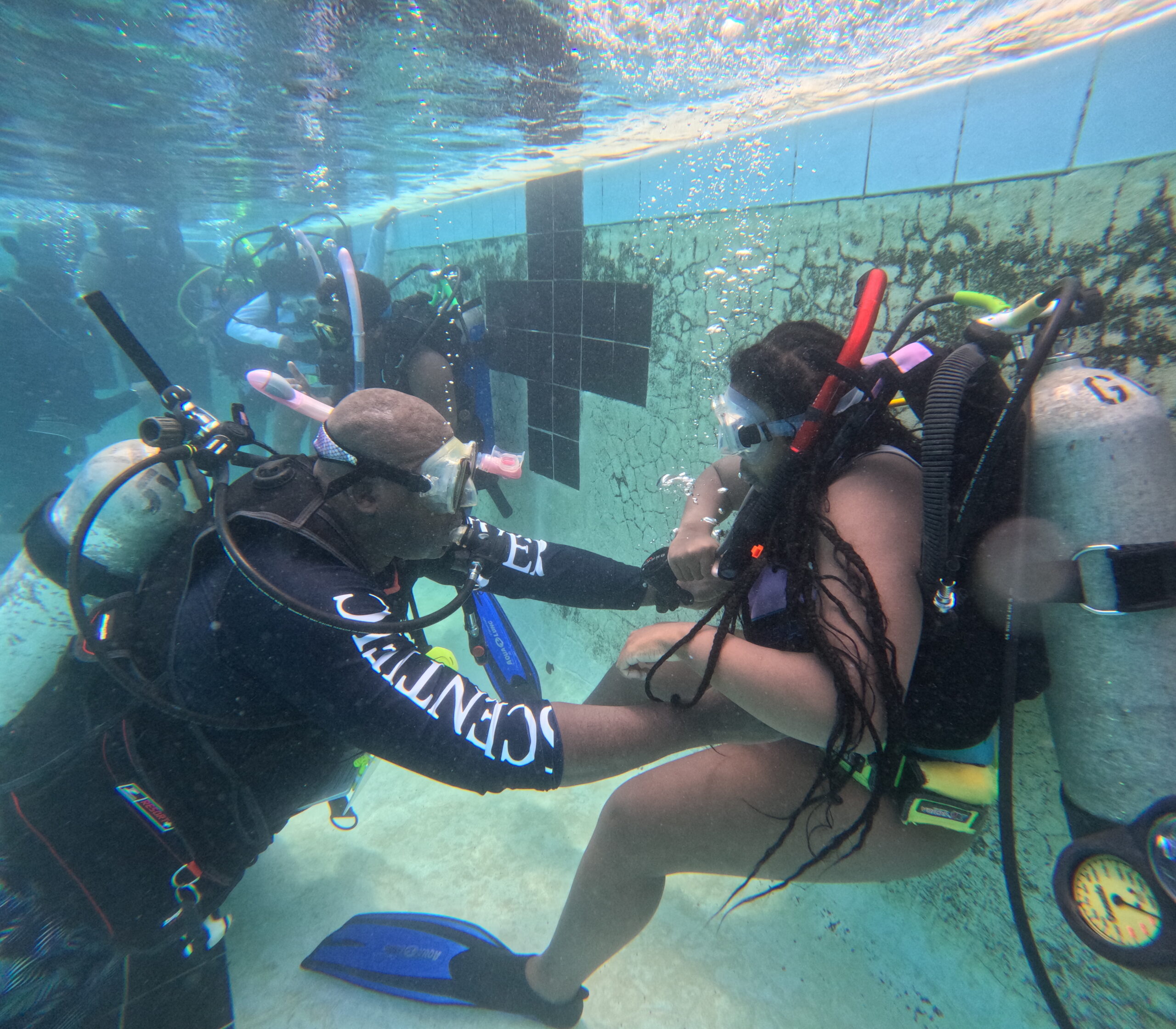 Man and woman underwater in a pool wearing full diving gear
