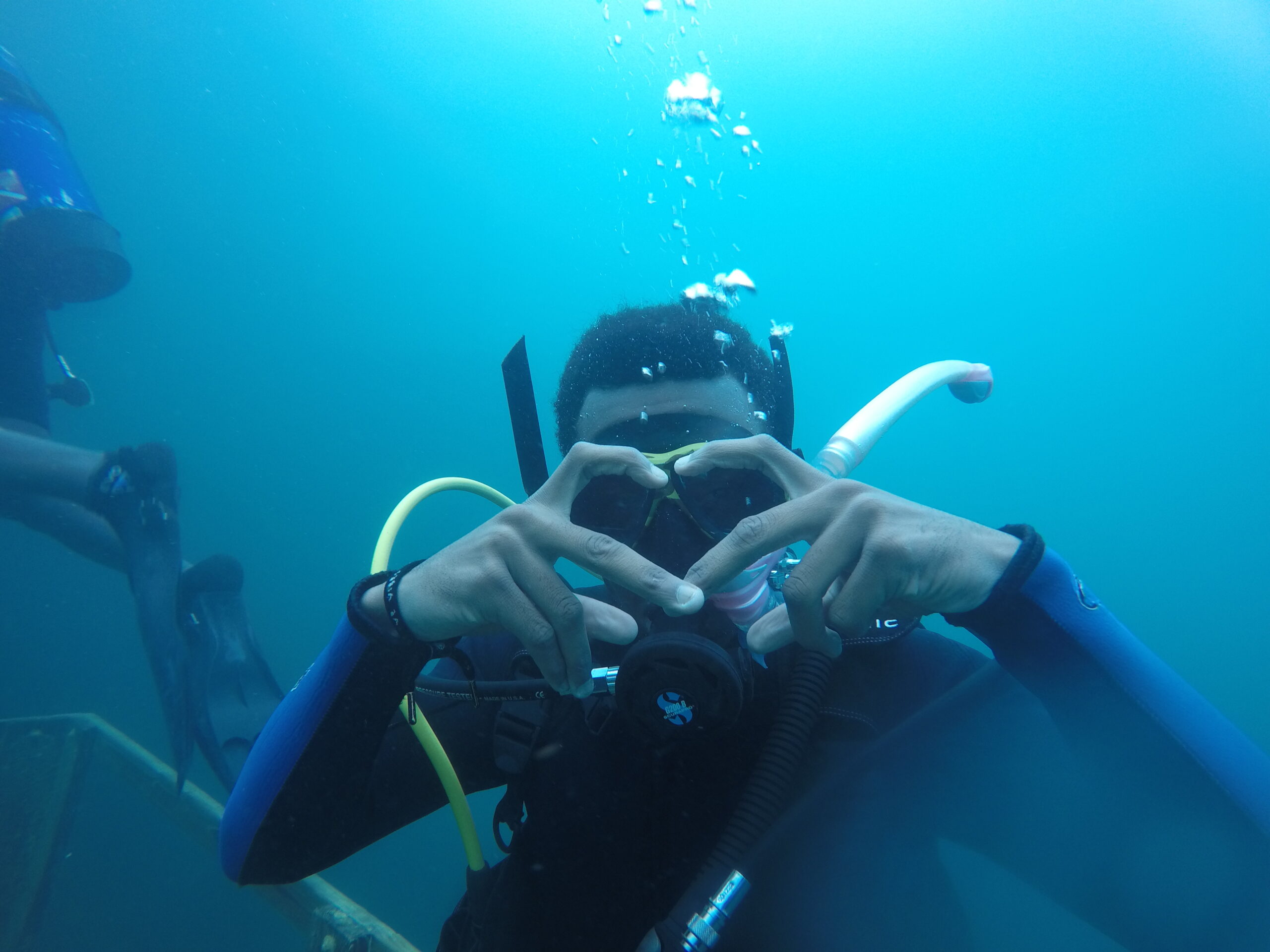 Man underwater making heart with hands while looking at Camera