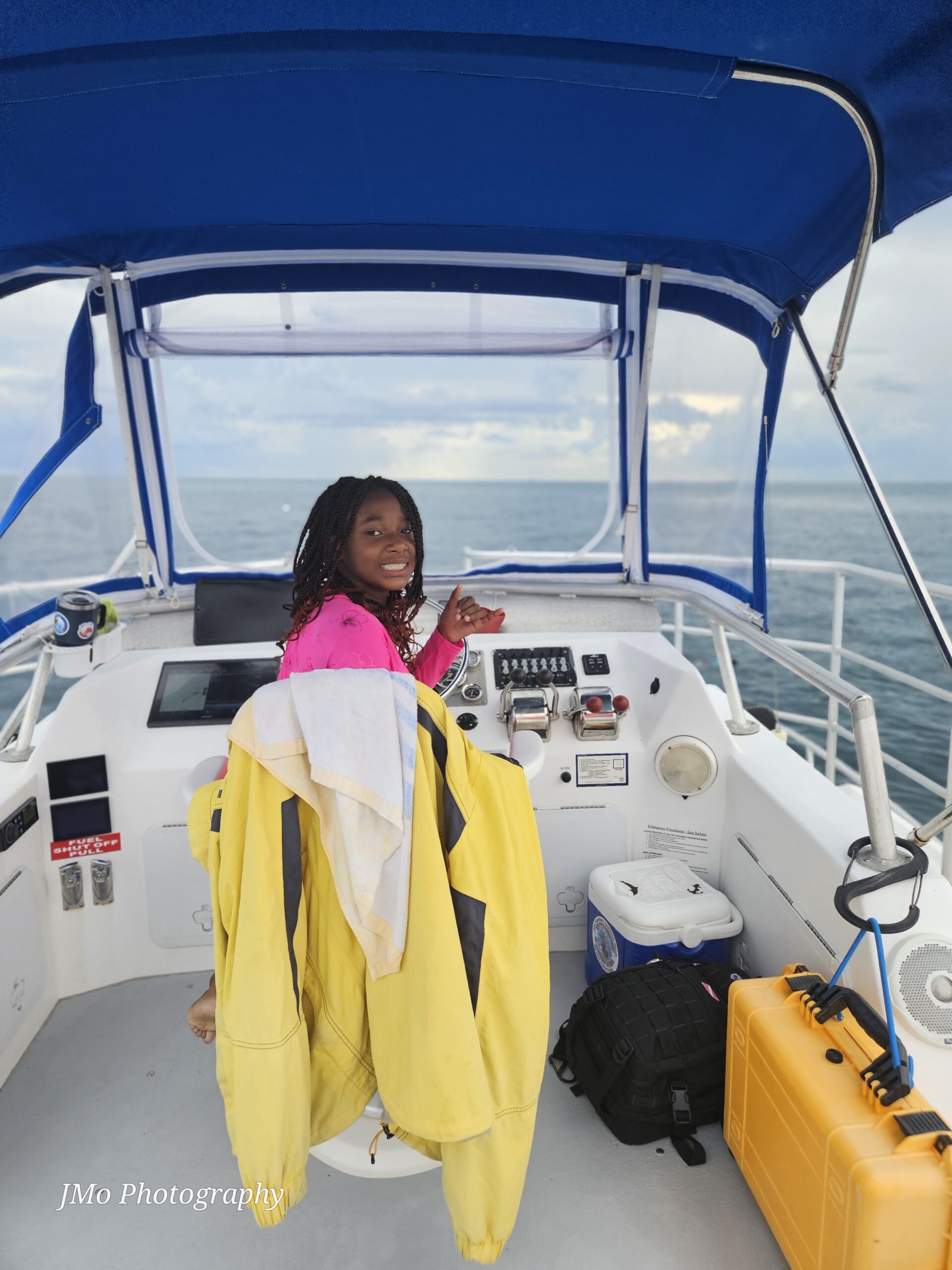 girl sits in caption's chair of boat smiling at the camera