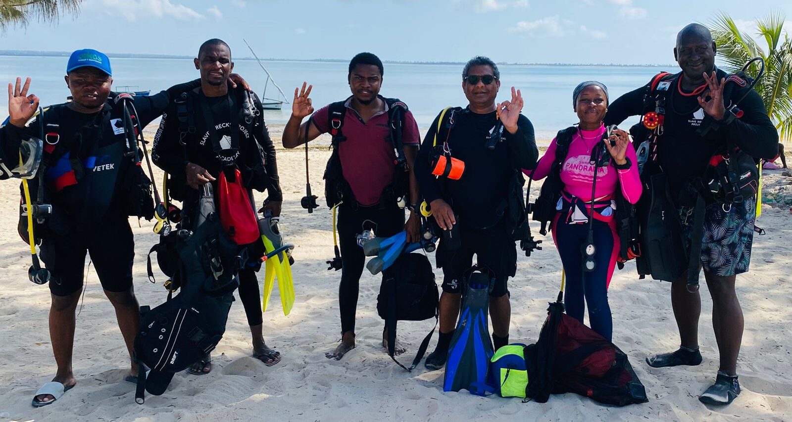 group of people smile at camera, standing on the beach.