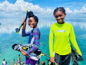 Two girls smile at the camera standing in front of the ocean