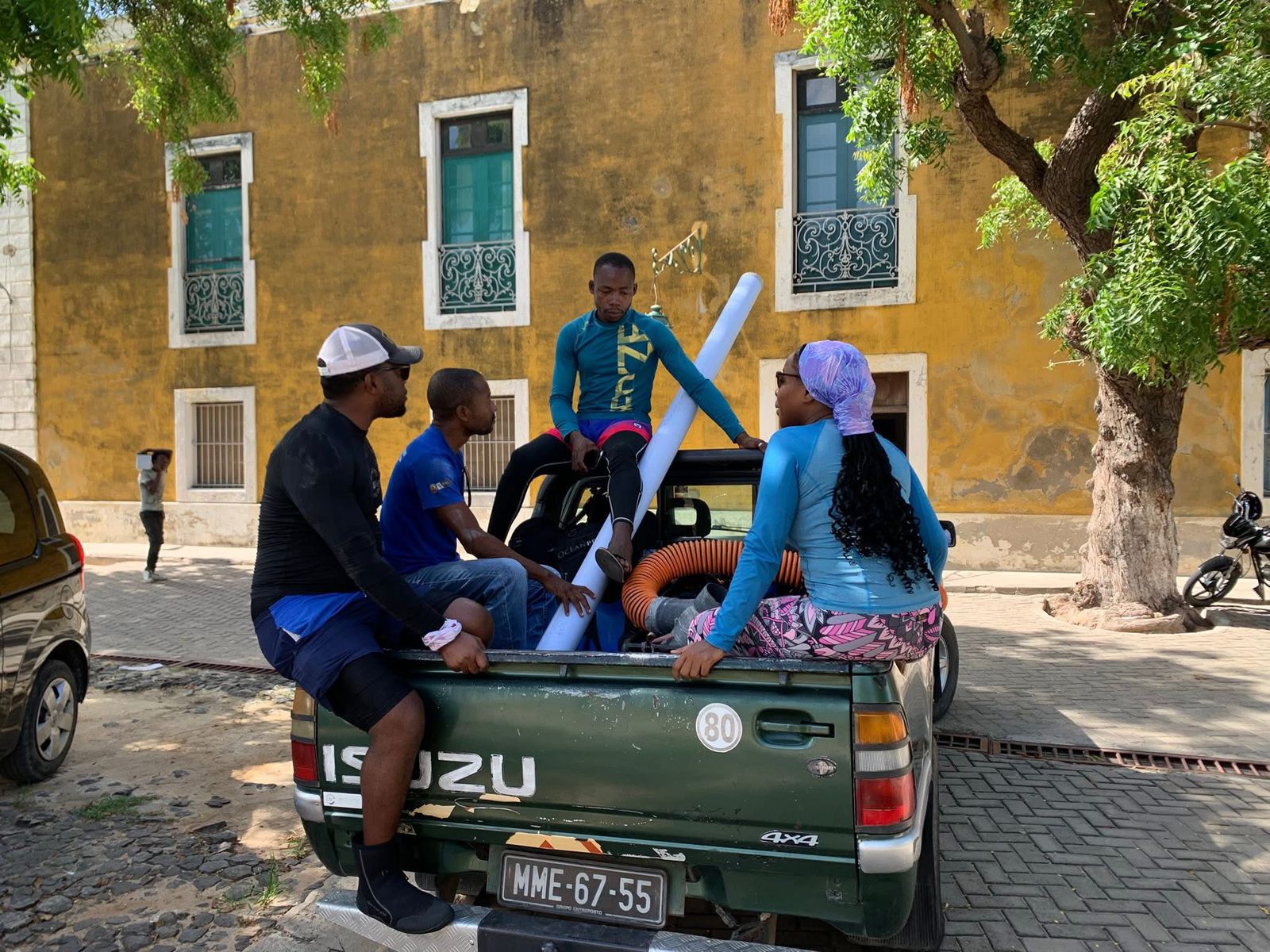Four people also sit in the bed of a truck facing away from the camera
