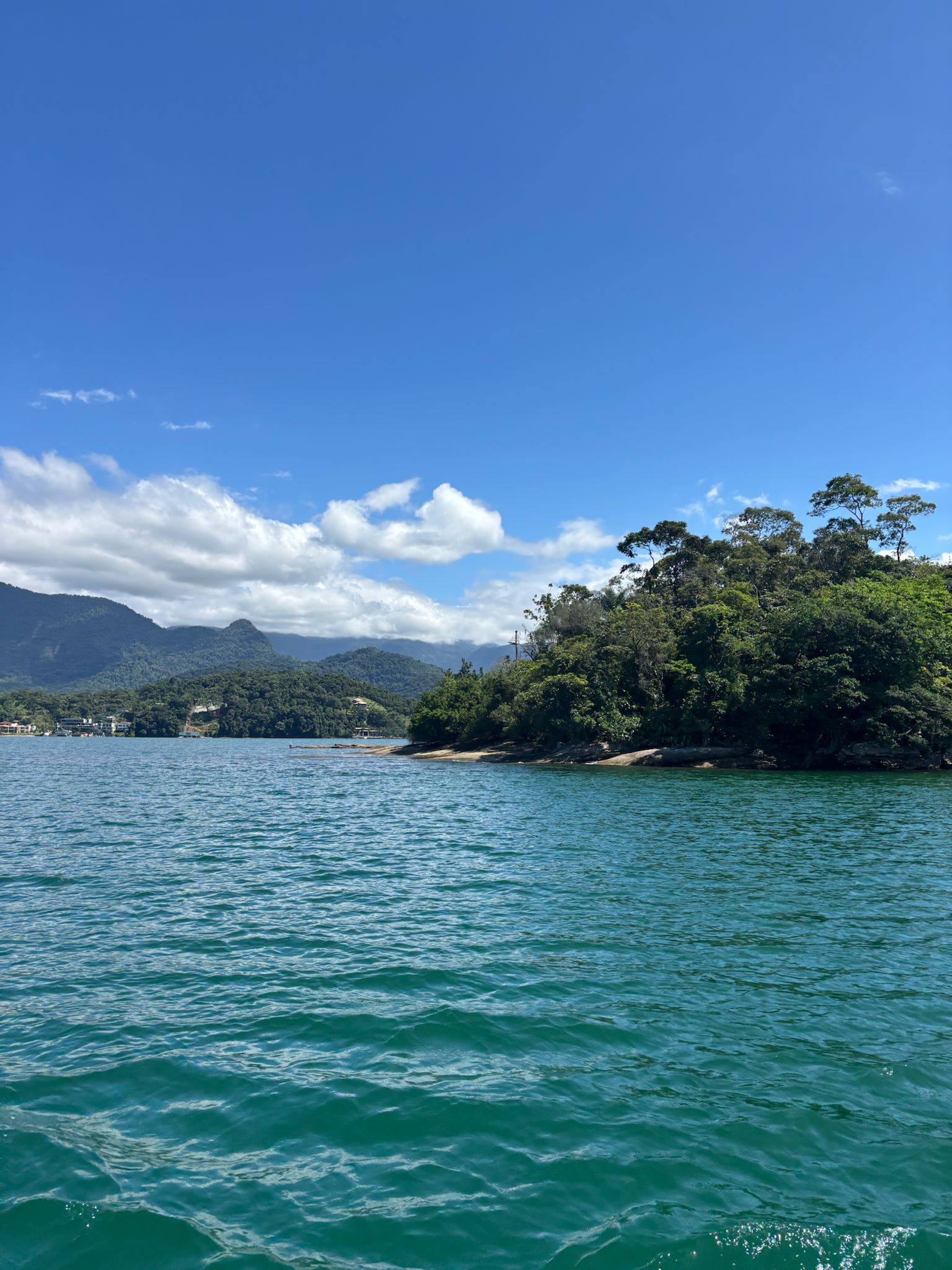 Beneath cloudless blue sky, a distant mountain and the shore are visible. The rest of the frame is filled with calm blue waters.